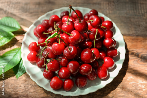 Plate with fresh ripe cherries on wooden background