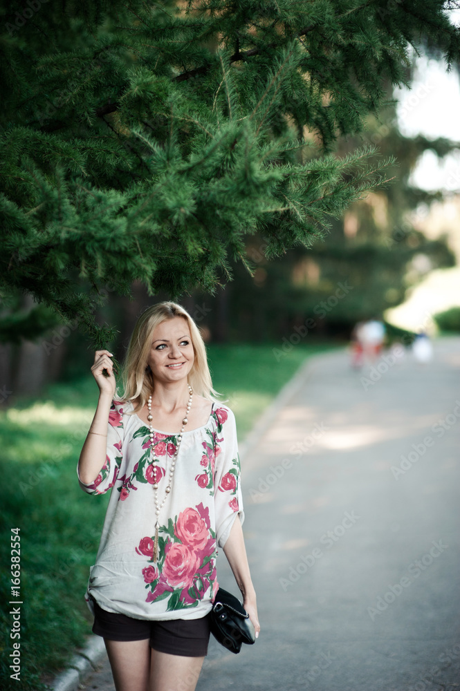 Blond girl in embroidery near a fur-tree on a walk