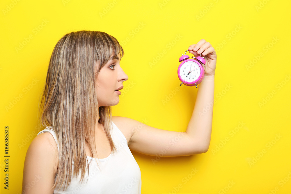Portrait of young woman with pink alarm clock on yellow background Portrait of young woman with pink alarm clock on yellow background