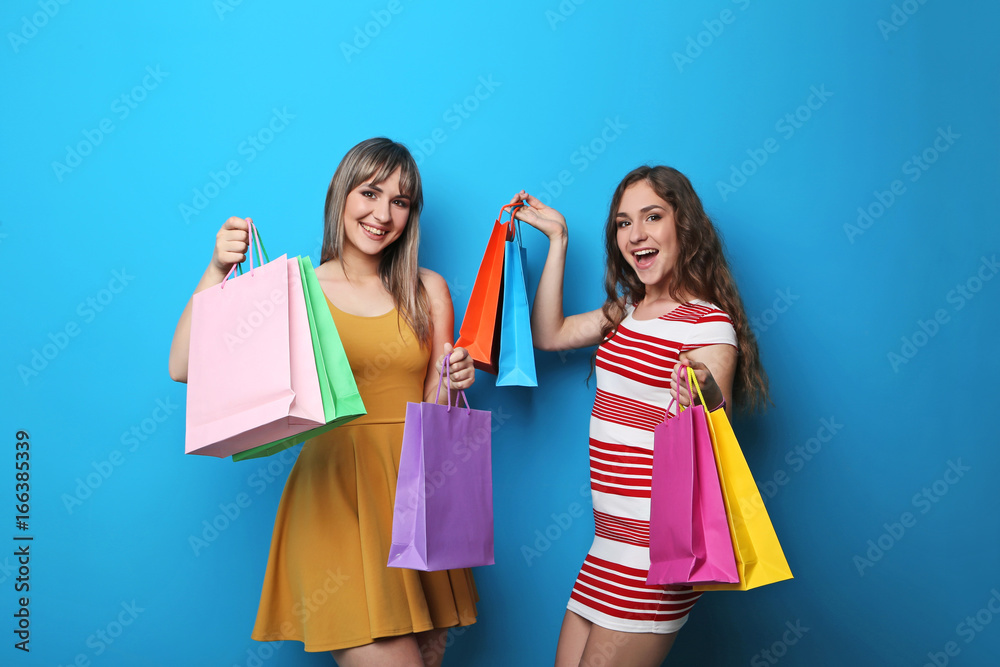 Portrait of two young woman with shopping bags on blue background