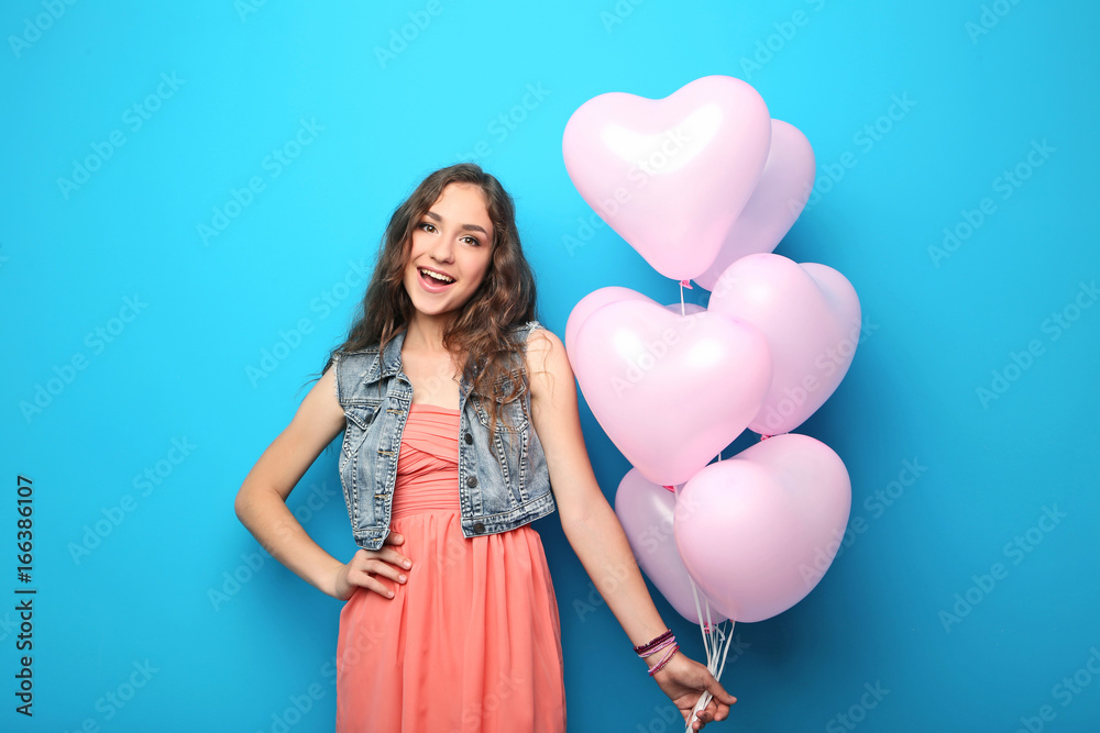 Portrait of young woman with pink heart balloon on blue background Portrait of young woman with pink heart balloon on blue background