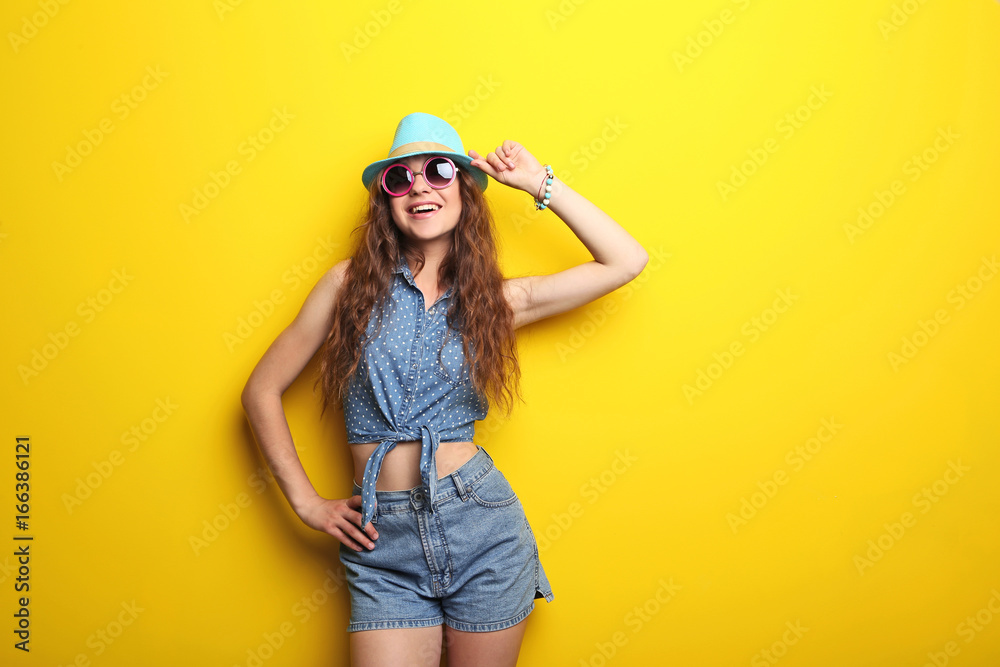 Portrait of young woman with hat and sunglasses on yellow background Portrait of young woman with hat and sunglasses on yellow background