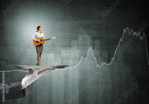 Attractive businesswoman on metal tray playing acoustic guitar and graphs at background