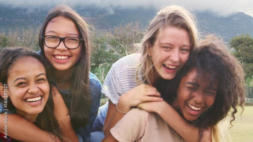 Four happy teenage girls piggybacking outdoors, close up