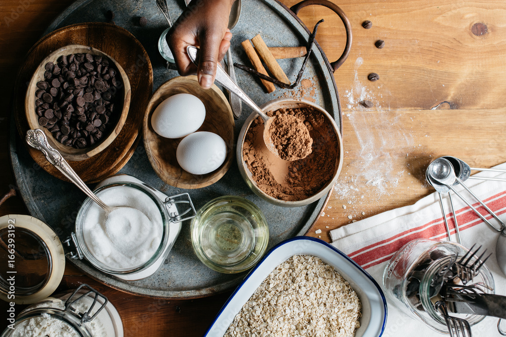 Hand of a black girl placing two eggs in a tray with cookie ingredients Hand of a black girl placing two eggs in a tray with cookie ingredients