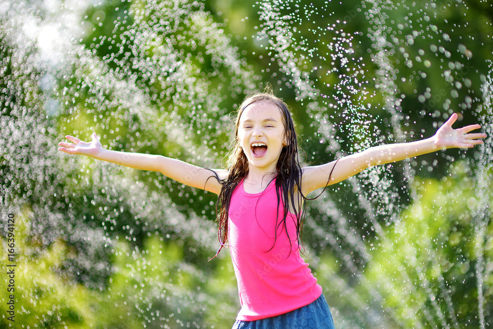 Adorable little girl playing with a sprinkler in a backyard on sunny summer day. Cute child having fun with water outdoors. Adorable little girl playing with a sprinkler in a backyard on sunny summer day. Cute child having fun with water outdoors.