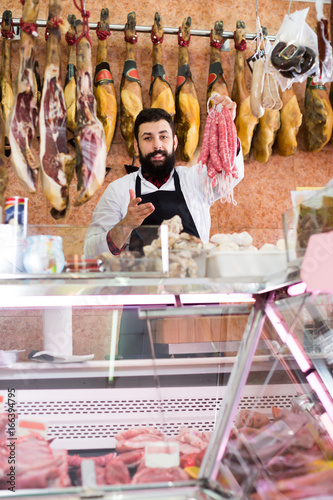 Smiling man seller showing different sausages