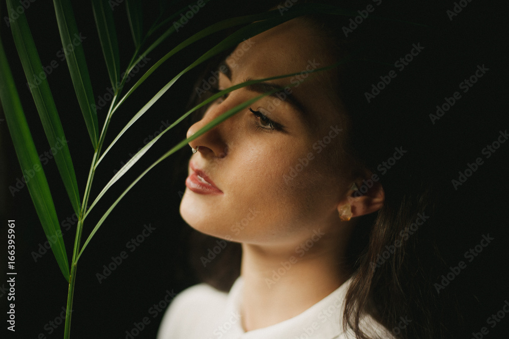 Female in dark room with window light and shadows with tropical green leaf
