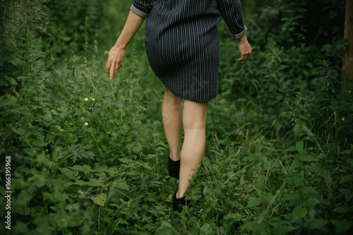 Woman in short dress and ankle boots walking in overgrown alleyway garden photo
