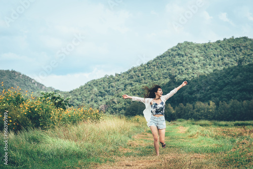 Happy young Asian woman running with arm raising outdoor to enjoy the nature with mountain in background