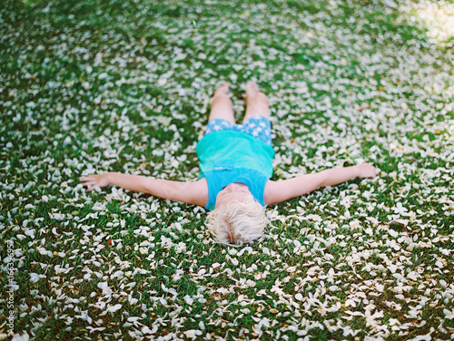 little boy in blue tank top and pjs and laying on bed of flower petals on green grass