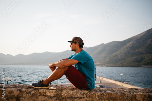 Young man sitting at a wall smoking a cigarette