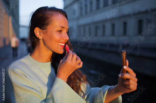 Attractive young girl paints lips in the light of the setting sun. deals lipstick on the lips