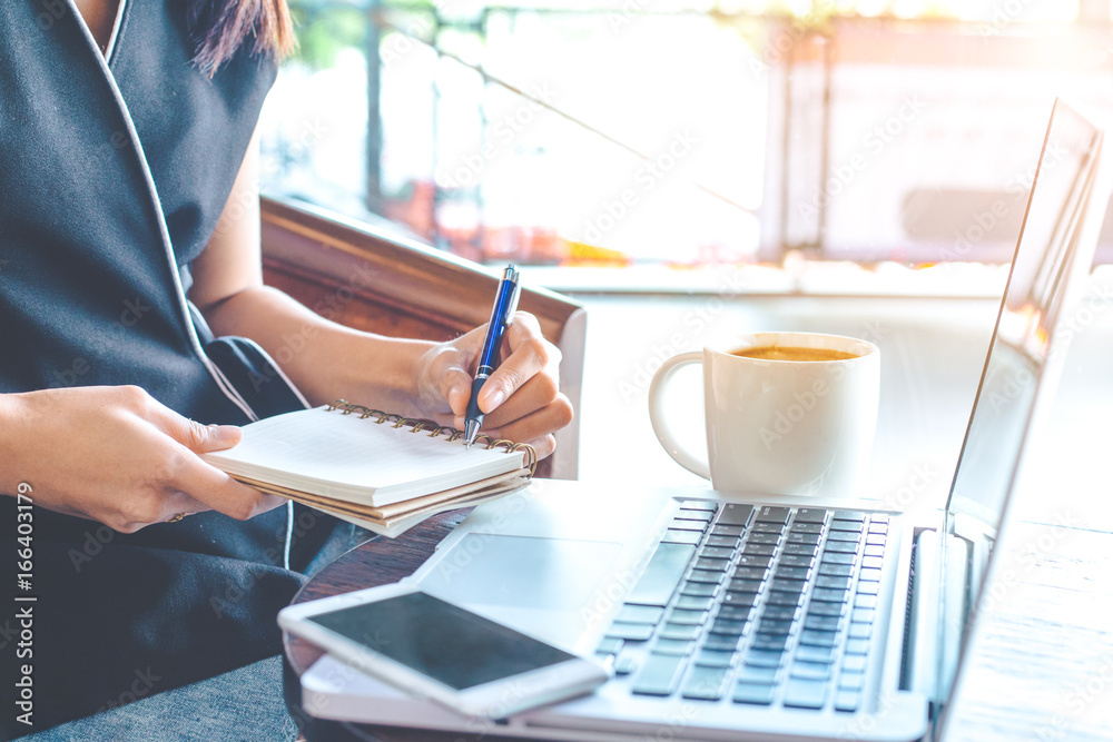 Business woman hand is working on a computer and writing in notepad.