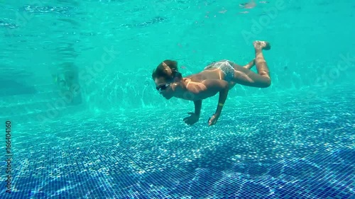 Caucasian swimmer child teen boy floats, dives in sunny pool with clear water at tourist resort. Active rest and healthy lifestyle, water sports in vacation holiday. Underwater survey, slow motion