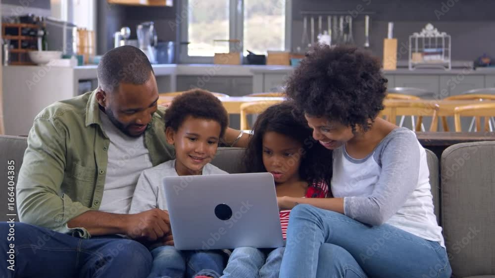 Family Sitting On Sofa In Open Plan Lounge Using Laptop
