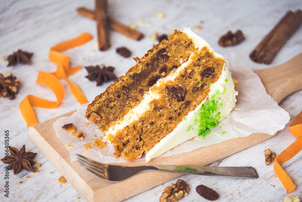 Close up of a homemade carrot cake with raisins, walnuts and cinnamon over white wooden background. Cream cheese frosting.