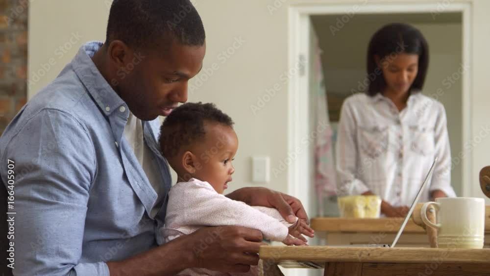 Father And Baby Daughter Use Laptop As Mother Prepares Meal Father And Baby Daughter Use Laptop As Mother Prepares Meal