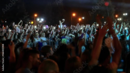Celebration in holiday, feast rejoicing. Night music concert, Lights and glare from searchlights. Disco show colorful illumination. Dancing crowd of youth, fans with hands up. 