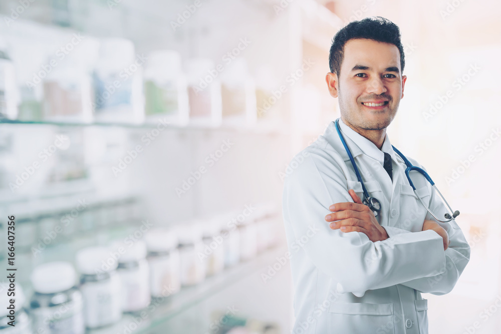 Asian smart doctor standing arms crossed and carrying stethoscope on shoulders at hospital with blurred drugstore background, concept of business advertising and consultation treatment patient. Asian smart doctor standing arms crossed and carrying stethoscope on shoulders at hospital with blurred drugstore background, concept of business advertising and consultation treatment patient.