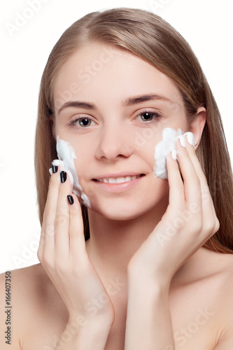 Beautiful woman cleaning face with foam treatment light background