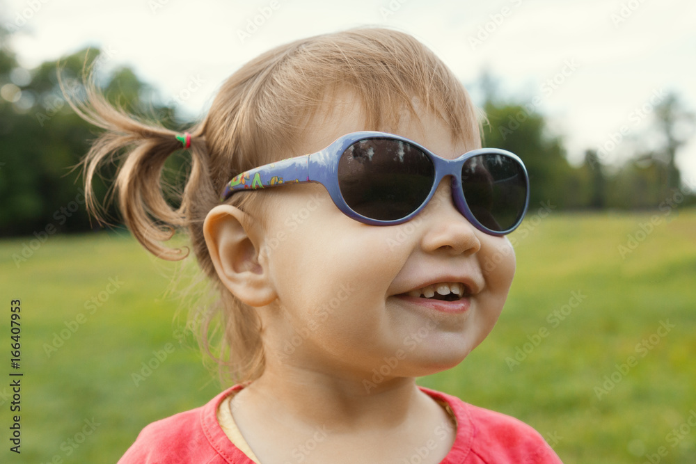 Little girl in sunglasses playing in park in front of green grass Little girl in sunglasses playing in park in front of green grass