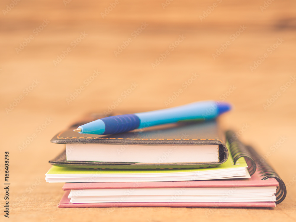 Naklejka premium Office accessories including note books and blue pen on wooden background. Education and business concept.