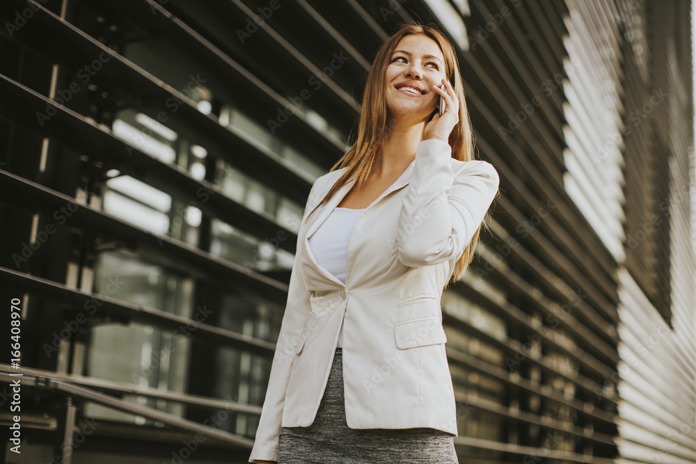 Fototapeta premium Pretty businesswoman with mobile phone in front of office building