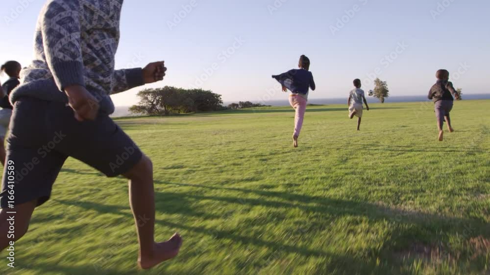 Elementary school kids chasing football in a field