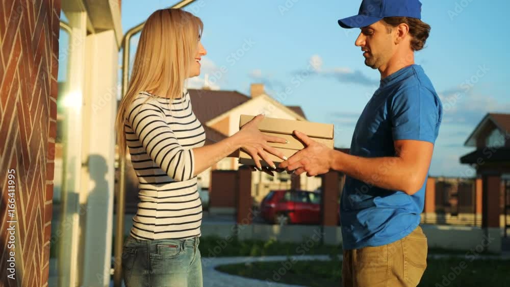 Attractive young woman signing the documents for getting package from the courier on the garden background. Side view. Attractive young woman signing the documents for getting package from the courier on the garden background. Side view.