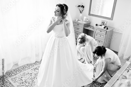 Bridesmaids helping gorgeous bride to dress up and get ready for her wedding ceremony. Black and white photo.