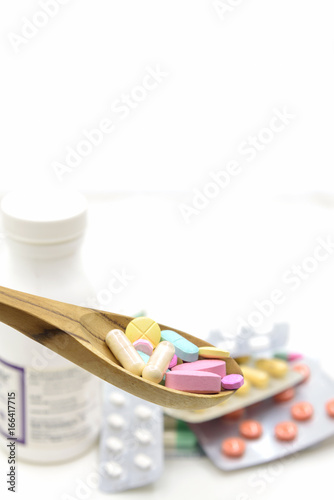 colorful tablet in wooden spoon & white pills medicine & bottle on white background photo