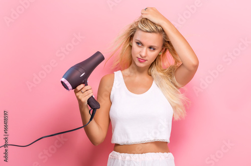 Beautiful woman holding a hairdryer on a pink background