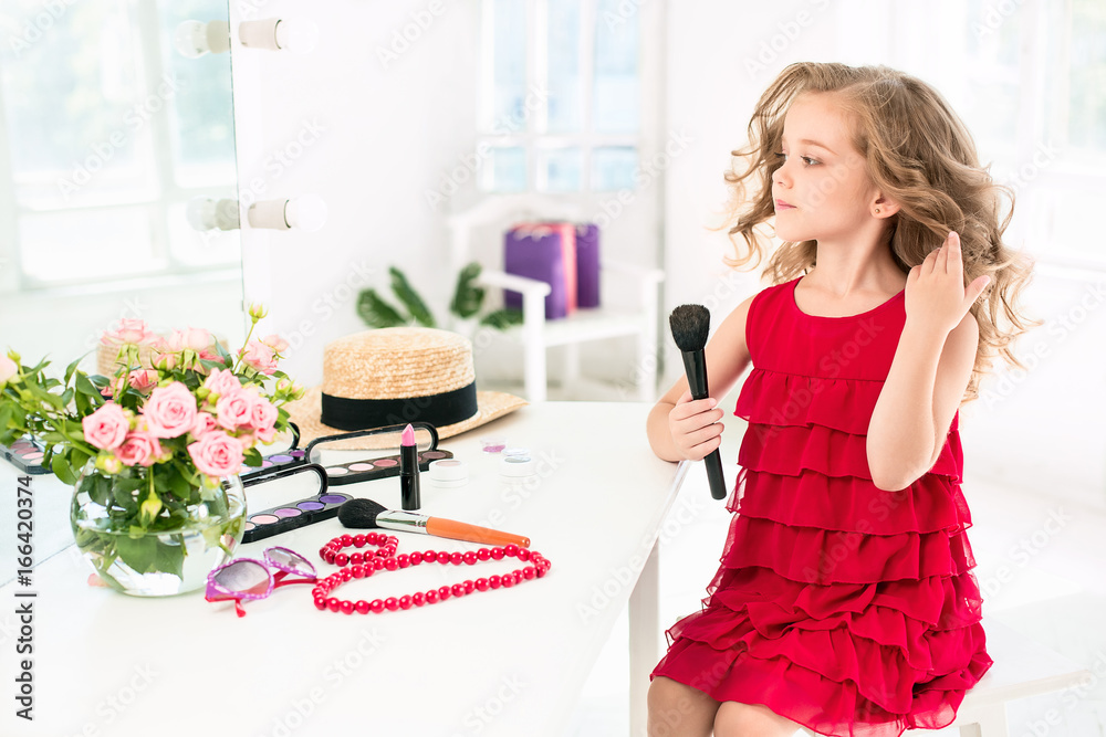 A little girl with cosmetics. She is in mother's bedroom, sitting near the mirror. A little girl with cosmetics. She is in mother's bedroom, sitting near the mirror.