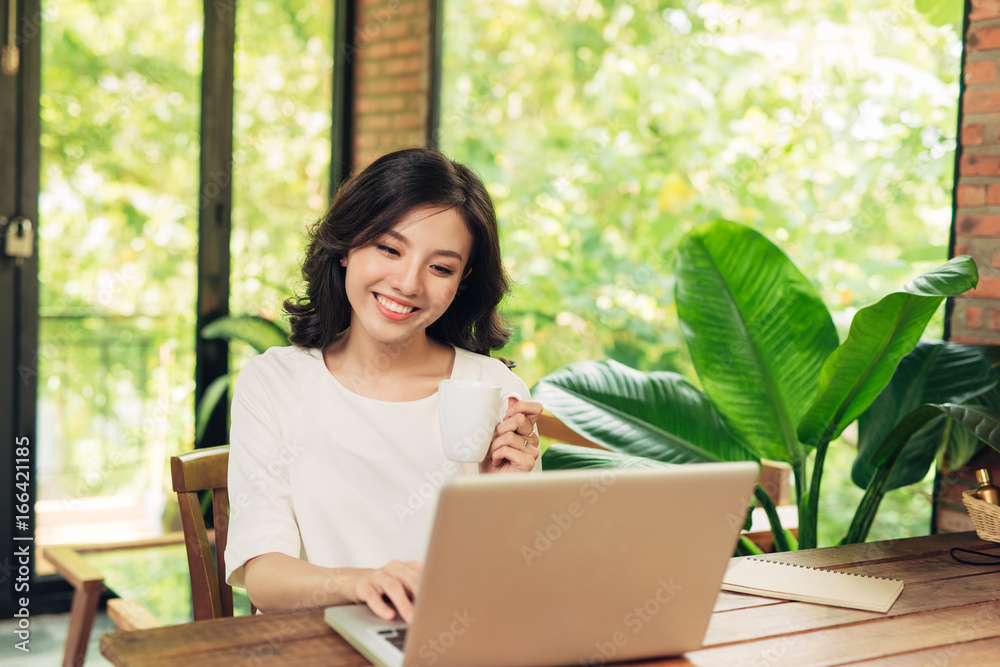 Beautiful young smiling woman working on laptop while sitting on bed at home near big window. Beautiful young smiling woman working on laptop while sitting on bed at home near big window.