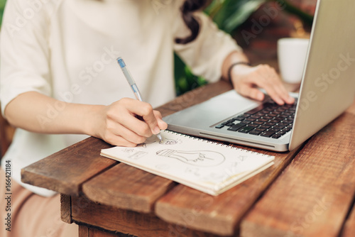 Young smiling asian woman sitting at table in cafe and writing in notebook