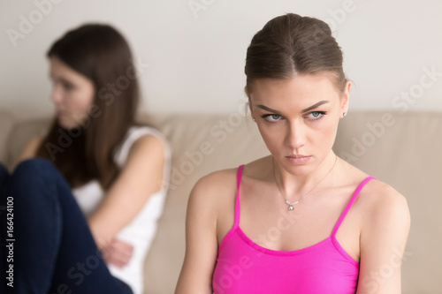 Headshot portrait of grumpy young woman sitting next to offended girlfriend after argument. Frustrated lady hating her friend  feeling wrath and dissatisfied because of conflict  ignores the opponent