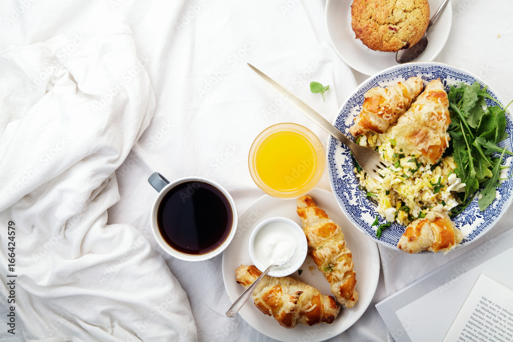 Breakfast in bed. Scrambled eggs with cheese croissants, raspberry muffin and black coffee. Lazy morning concept. Flat lay with copy space. Breakfast in bed. Scrambled eggs with cheese croissants, raspberry muffin and black coffee. Lazy morning concept. Flat lay with copy space.