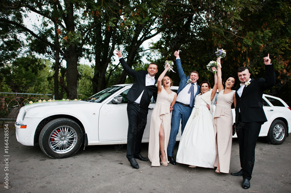 Wedding couple and groomsmen with bridesmaids posing next to the limousine.