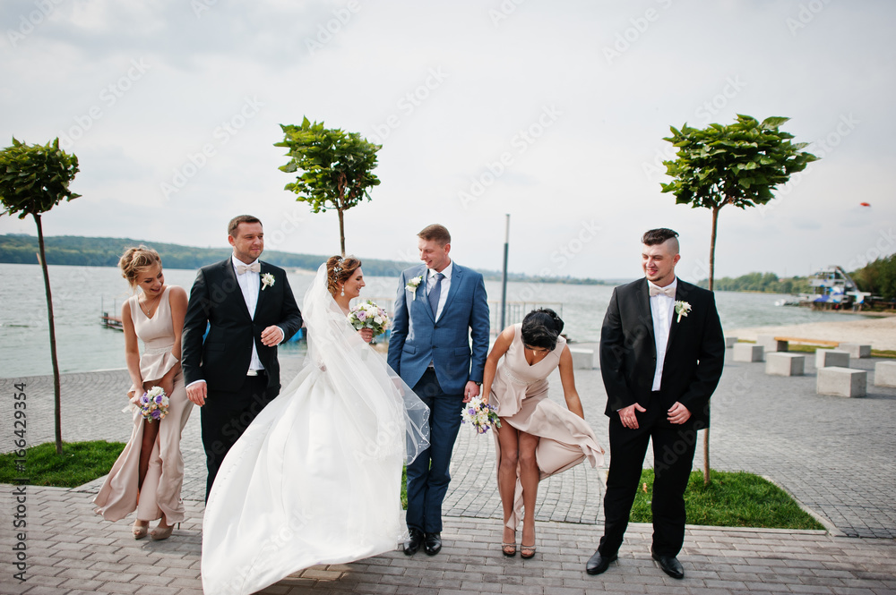Amazing wedding couple and crazy groomsmen with bridesmaids having fun on the lakeside.