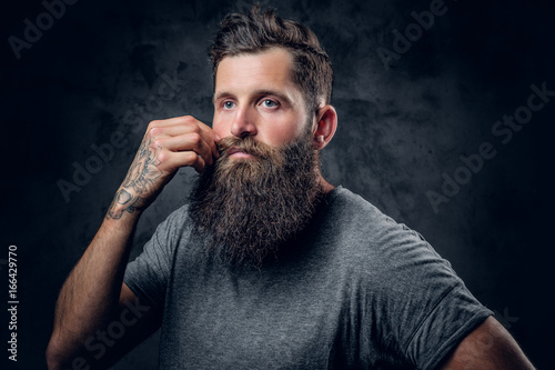 A man touches his moustache over grey background.