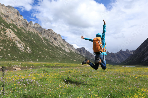 cheering young backpacking woman jumping on flowers and grass