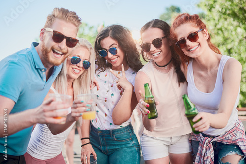 Friends posing at outdoor party while standing and drinking alcohol