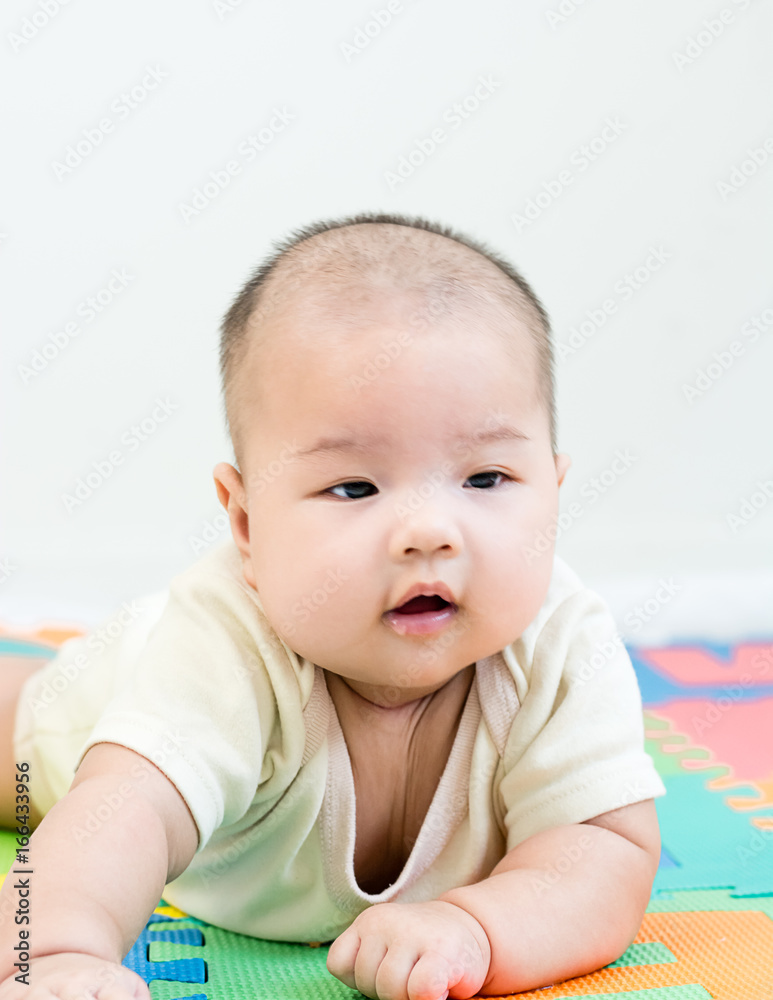 Portrait of a little adorable infant baby girl lying on the tummy on colorful eva foam indoors