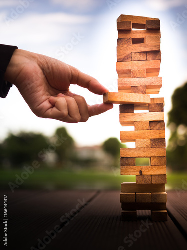 hand of businessman pulling out or placing wood block on the tower. plan and strategy in business. blur for background
