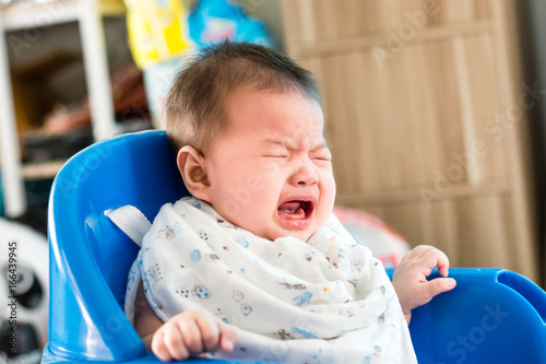 Portrait of adorable infant baby girl sitting on the chair and crying while eating baby food