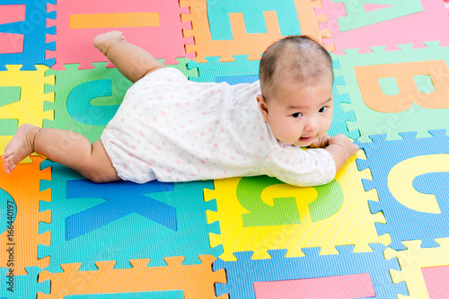 Portrait of a little adorable infant baby girl lying on the tummy on colorful eva foam indoors