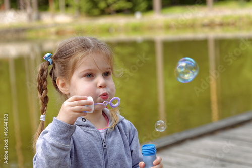 Adorable little girl blowing bubbles in the park.