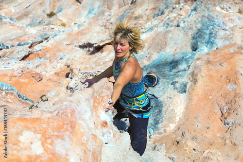 Portrait of adult Female Rock Climber moving up on difficult Wall