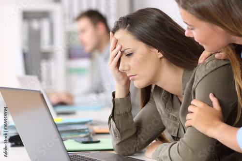 Sad employee being comforted by a colleague photo